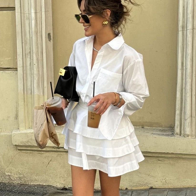 Camisa blanca de manga larga con cuello solapa y vestido de cintura alta con diseño de capas.